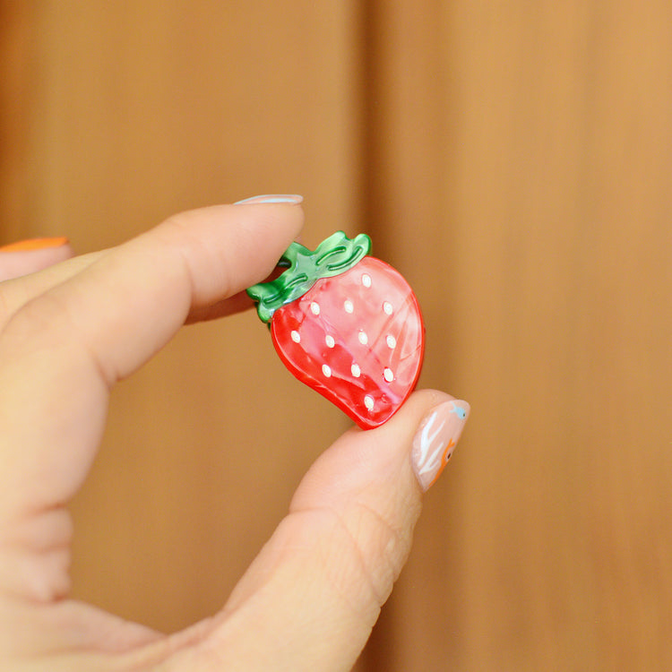 Hand holding a strawberry shaped hair clip against a wooden background