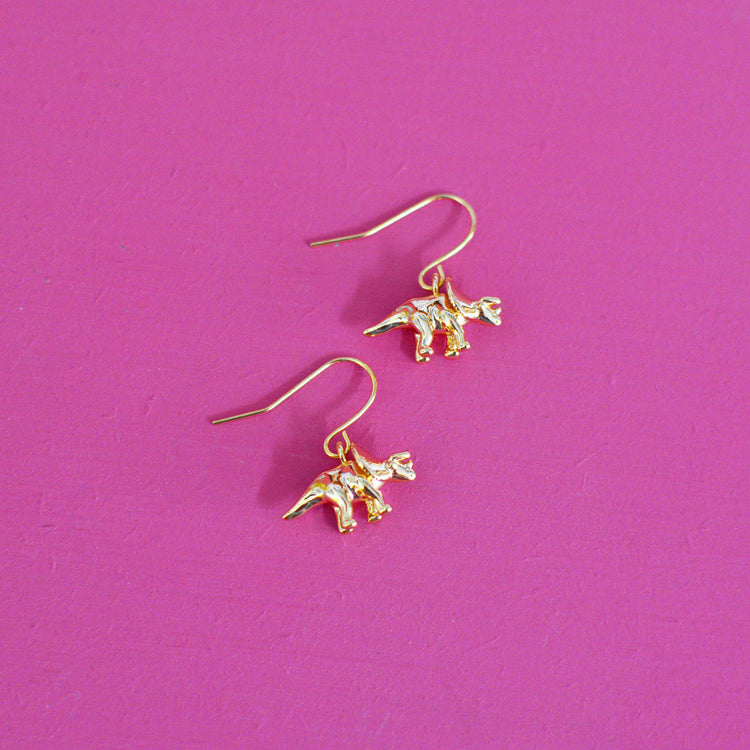 Gold plated triceratops dinosaur earrings with hooks on a pink background