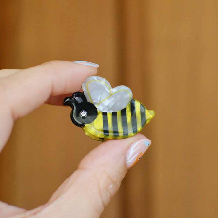 Hand holding a small bee-shaped hair claw clip against a wooden background