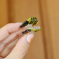 Hand holding a small bee shaped hair clip against a wood background. The claw is held open so you can see the tiny transparent teeth inside.