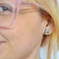 A picture of a woman with blonde hair and pink glasses revealing her earlobe wearing a Mr Blobby stud earring that features his pink face with yellow spots, big green eyes and a cheesy grin.