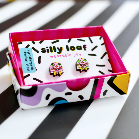 Mr Blobby stud earrings displayed on a white card with Silly Loaf branding and a sticker that says "hypoallergenic stainless steel". The card is presented in a colourful gift box.