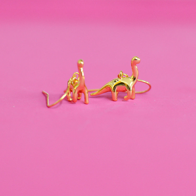 Gold dinosaur shaped earrings with long necks on a pink background