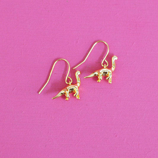 Gold plated brontosaurus dinosaur earrings with hooks on a pink background