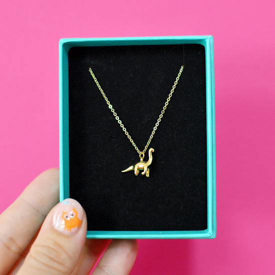 Gold plated dinosaur necklace in a gift box against a pink background