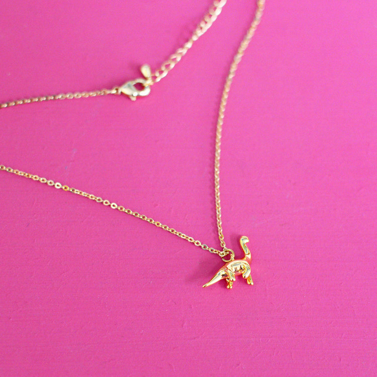 Gold plated necklace with a brontosaurus pendant on a pink background