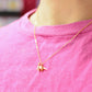 Gold plated necklace with a small long necked dinosaur pendant being worn over a pink shirt