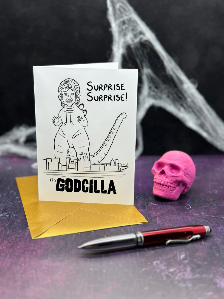 Greeting card with a Godcilla illustration (a mash up of Godzilla and Cilla Black), pink skull, and pen on a dark background