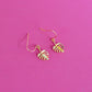 Gold leaf shaped earrings with hooks on a pink background