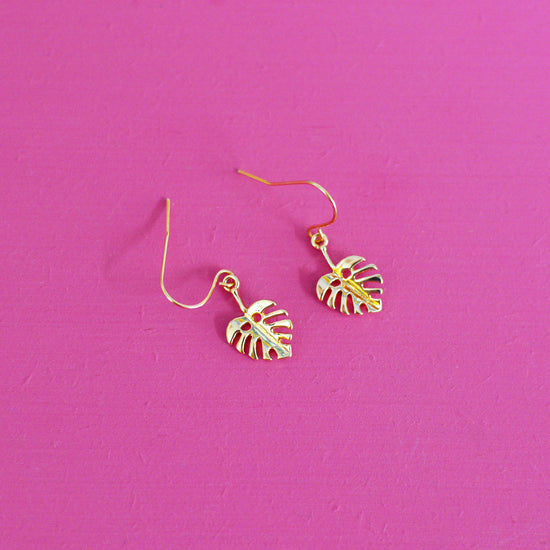 Gold leaf shaped earrings with hooks on a pink background