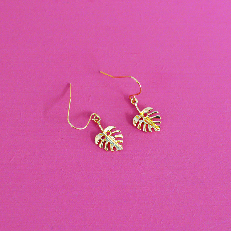Gold leaf shaped earrings with hooks on a pink background