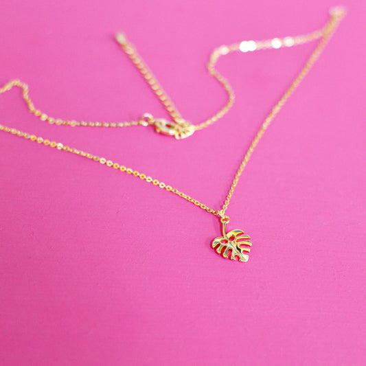 Gold plated necklace with a monstera leaf pendant, laid out with the fine chain and lobster clasp visible on a pink background