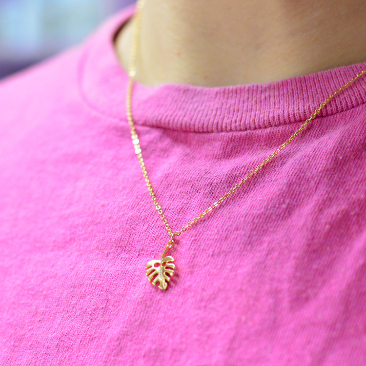 Gold plated necklace with a cheese plant leaf pendant on a pink shirt