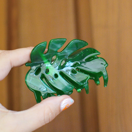 Green leaf shaped hair claw clip held by a hand against a wooden background