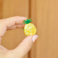Hand holding a small pineapple-shaped hair claw clip against a wooden background