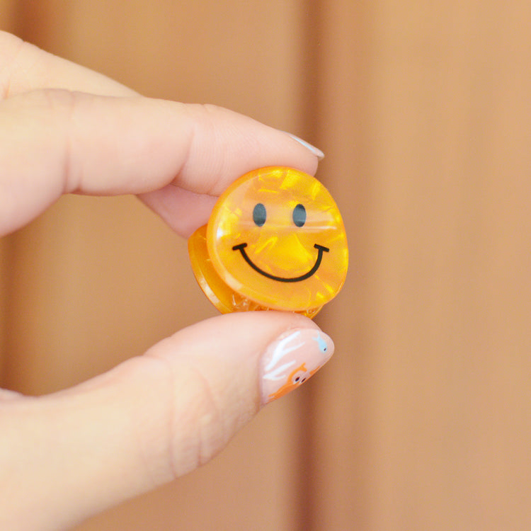 Hand holding a small orange smiley face hair clip against a wooden background