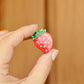 Hand holding a strawberry shaped hair clip against a wooden background