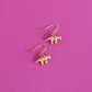 Gold plated triceratops dinosaur earrings with hooks on a pink background
