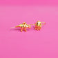 Gold plated triceratops shaped earrings on a pink background