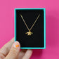 Gold plated dinosaur necklace in a gift box against a pink background