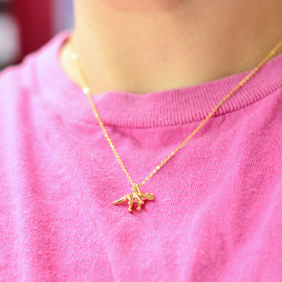 Gold plated necklace with a small dinosaur pendant shown being worn with a pink t-shirt