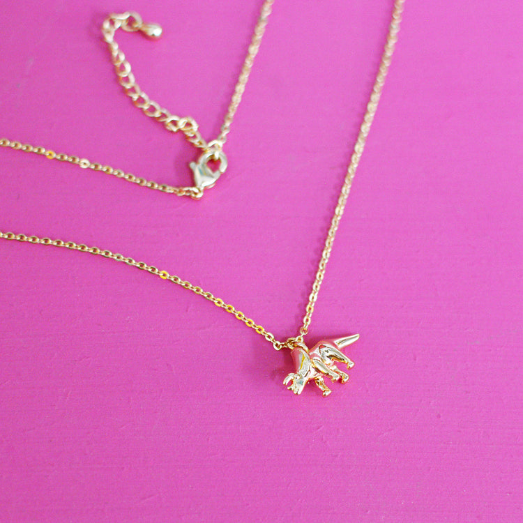 Gold plated necklace with a triceratops pendant on a pink background with the fine chain and lobster clasp visible.
