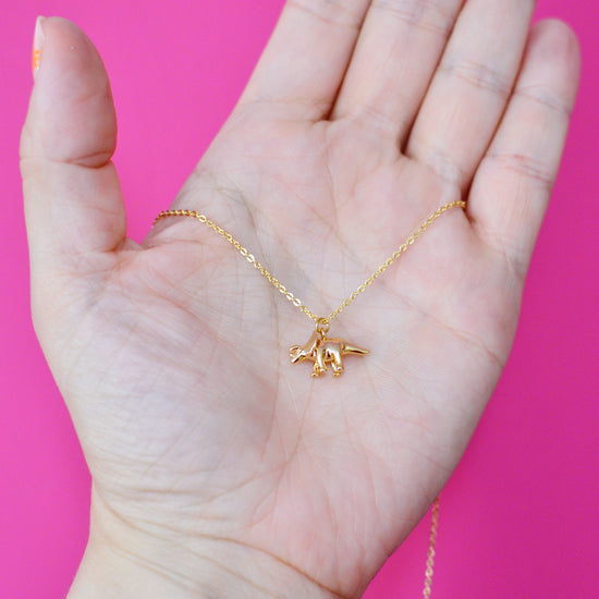 Triceratops dinosaur necklace held in a hand to show it is quite small and dainty.