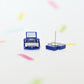 Small blue typewriter stud earrings on a white background with colorful abstract elements. You can see the whole of one stud earring and the back of the other which reveals the earring post.